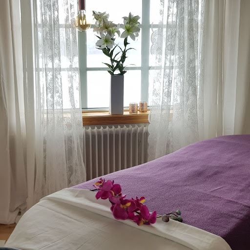 Massagebädd med orkidé på, framför fönster med spetsgardiner.