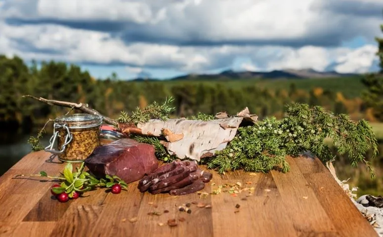 Uppskuret kött på skärbräda, med fjällvy i bakgrunden.