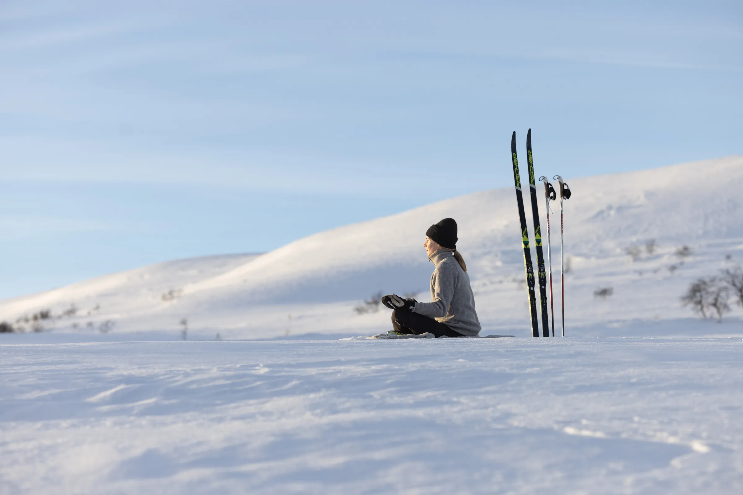 Kvinna sitter i yogaställning i snön, med längdskidor bredvid sig.