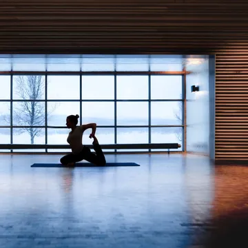 Person som utför yoga framför ett stort fönster med utsikt över ett snötäckt landskap.