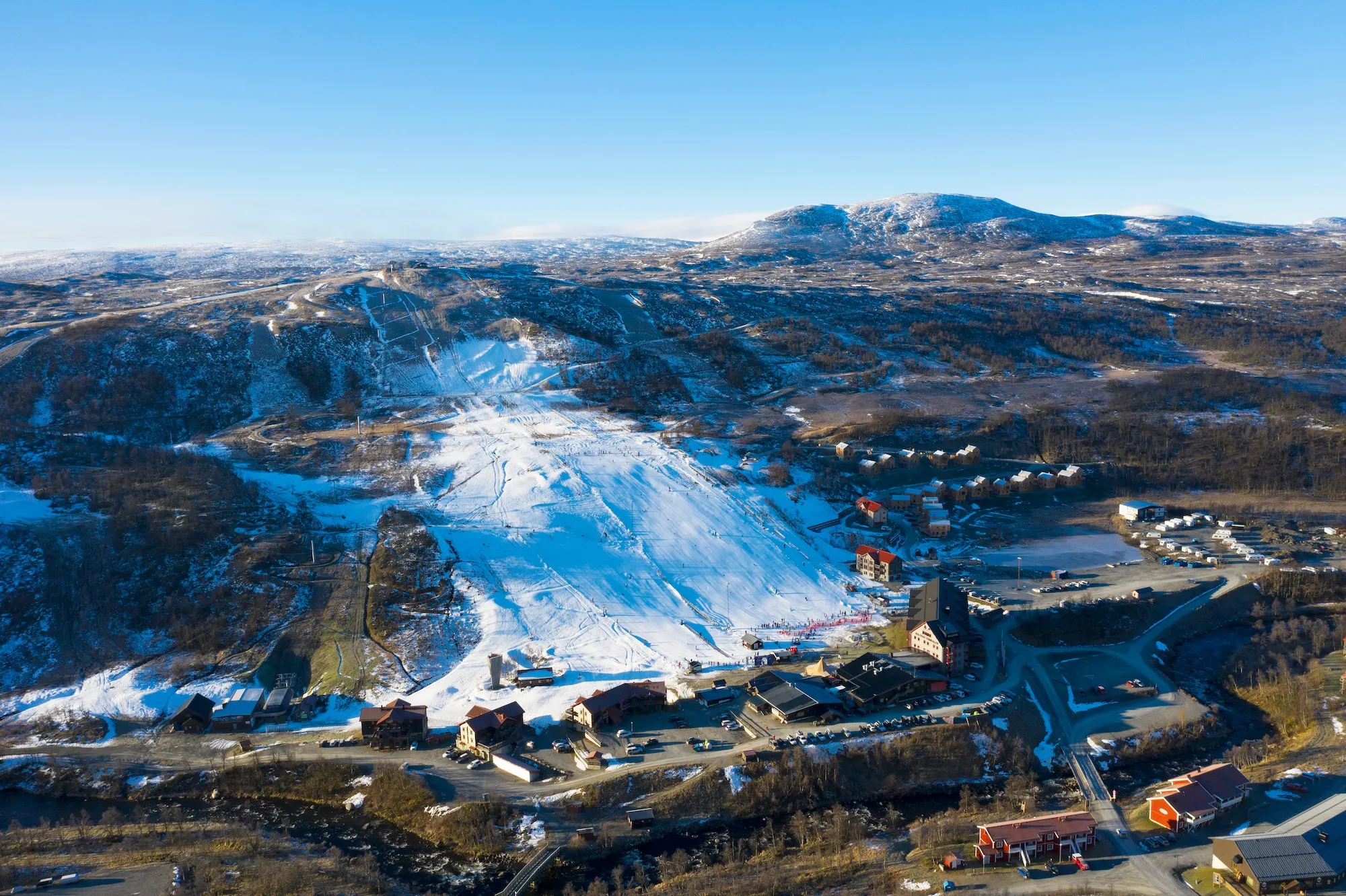 Pistad skidbacke i Tänndalen med sparad snö. Snöfritt utanför skidbacken.