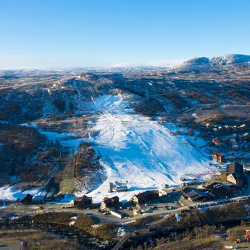 Pistad skidbacke i Tänndalen med sparad snö. Snöfritt utanför skidbacken.